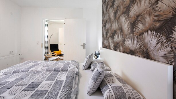 A bedroom with a patterned bedspread, a large wall art piece, and a door leading to another room. - Apartment 'Ferienwohnung Steffi' with Private Terrace and Wi-Fi (Laichingen)