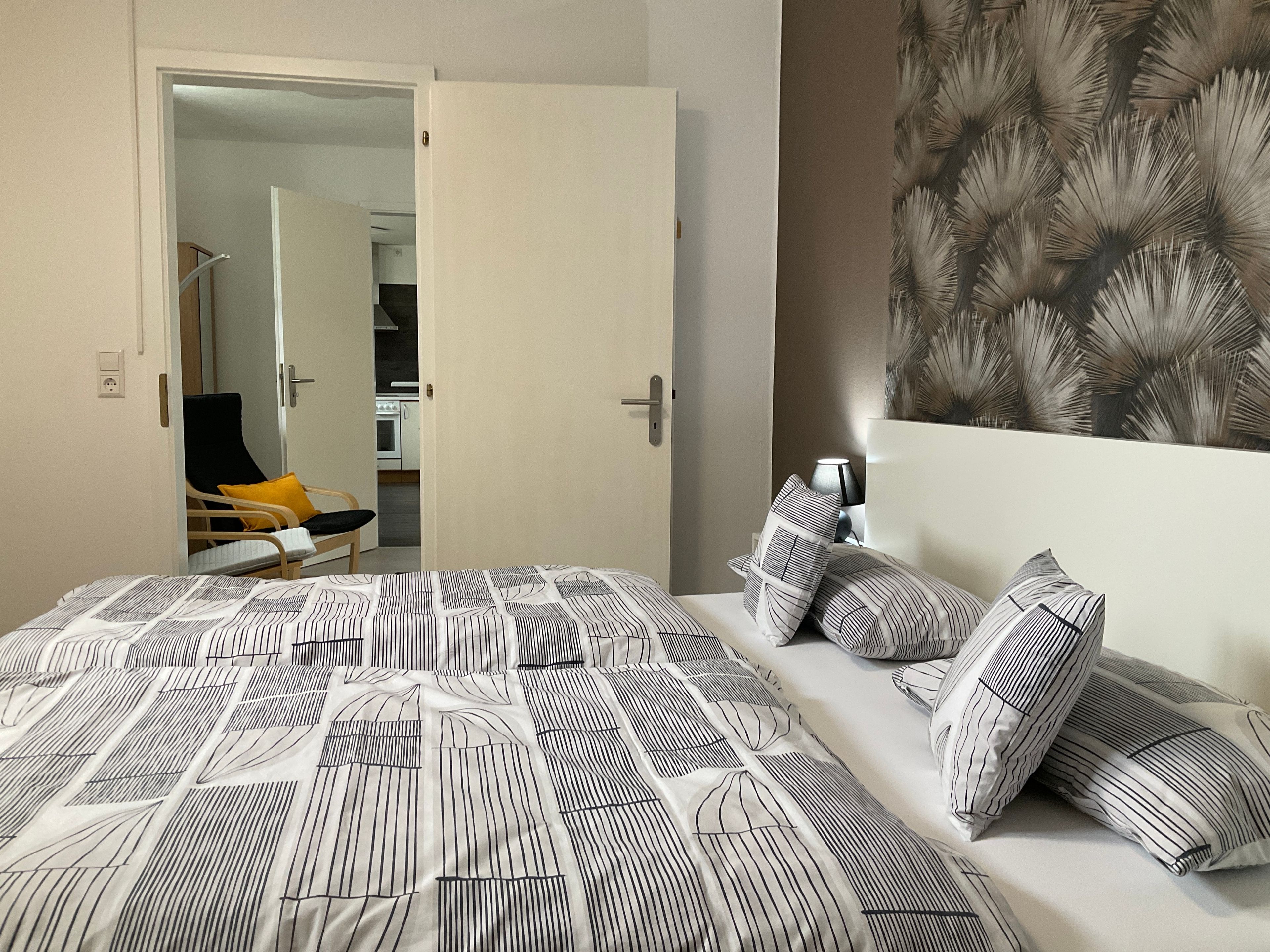 Ein Schlafzimmer mit Bett, Nachttisch und Blick zur Küche.