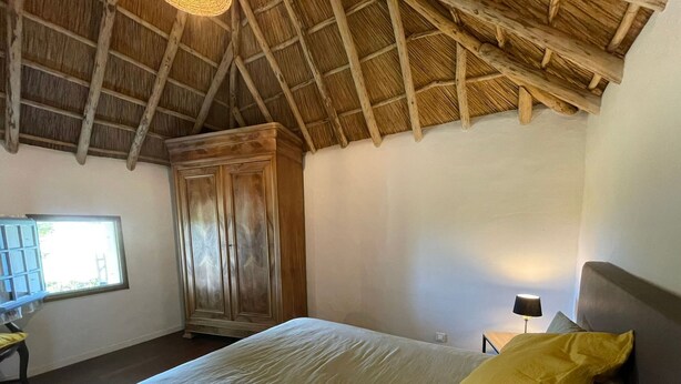 Een slaapkamer met een houten plafond, een bed met een geel kussen, een kledingkast en een nachtkastje met een lamp.