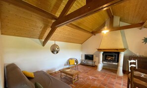 A cozy living room with a wooden ceiling, a fireplace, a sofa, and a television.