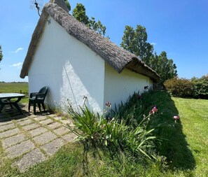 A small white building with a thatched roof, a table, and chairs outside.