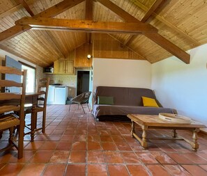 A rustic interior with a wooden ceiling, tiled floor, a sofa, a dining table, and a kitchen area.