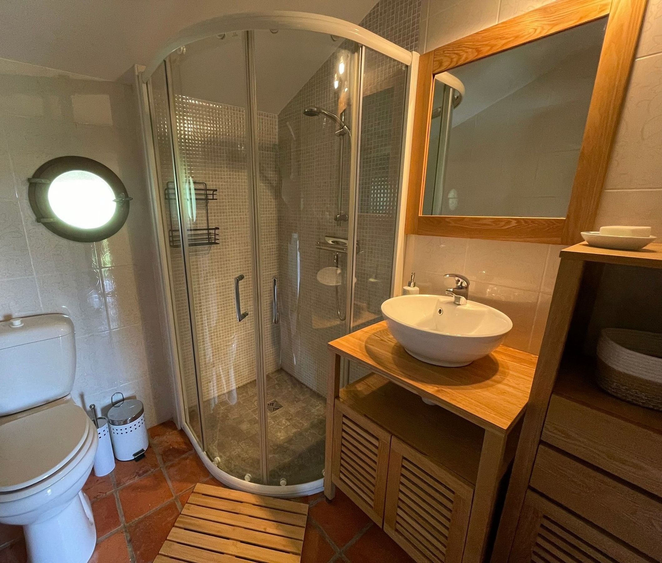 Een badkamer met een toilet, een douche met glazen wand, een wastafel en een spiegel.