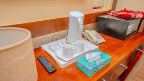 Habitación de hotel con un mostrador de madera, una cafetera, un teléfono, un control remoto y una caja de pañuelos.