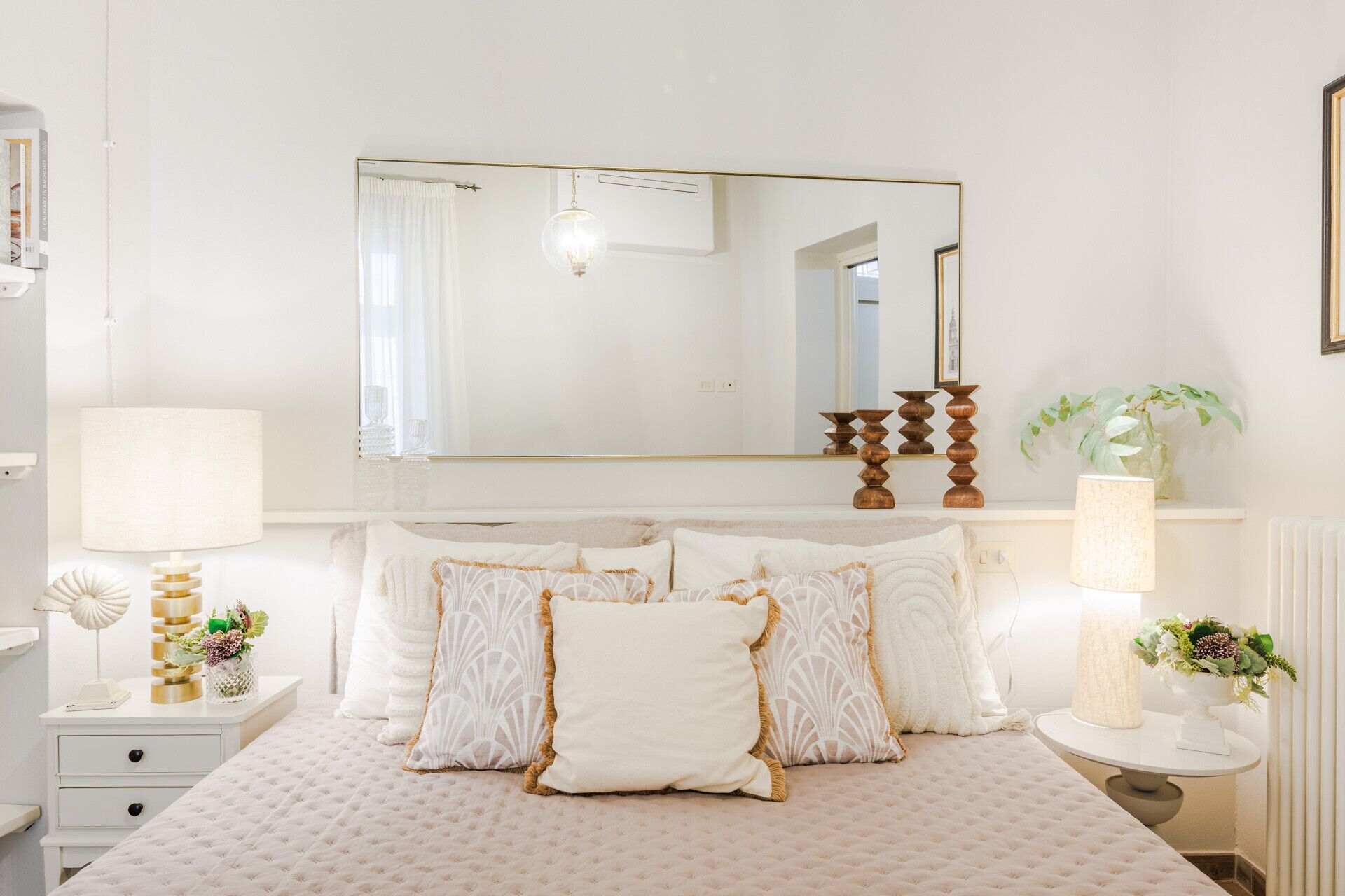 A neatly arranged bedroom with a large bed, bedside tables, a mirror, and a radiator.