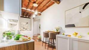 Una cocina moderna con una isla de madera, armarios blancos y un techo rústico. Hay dos taburetes de bar y una mesa de comedor con un jarrón de flores.