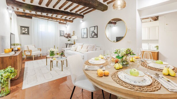 Un salón comedor bien iluminado, con techo de madera, paredes blancas y un espejo redondo.