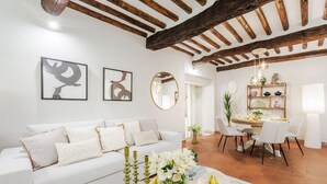 Una sala de estar moderna con un sofá blanco, un comedor con una mesa redonda y una cocina a la vista al fondo.