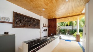 A reception area with a wooden ceiling, a large decorative panel, a reception desk, and a view of the outdoor garden. - JR Siam Hotel (Karon)