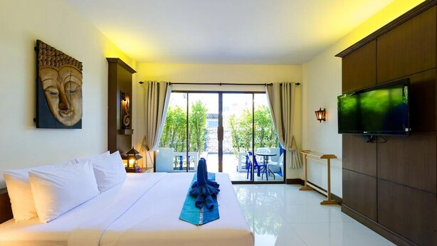 A hotel room with a bed, a TV, a large window, and a view of the outdoors. - JR Siam Hotel (Karon)