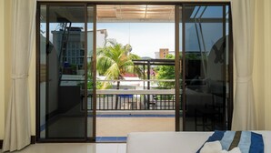 A hotel room with a sliding glass door leading to a balcony with a view of palm trees and buildings. - JR Siam Hotel (Karon)