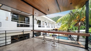 A balcony with a pool, two bar stools, and a view of a boat and palm trees. - JR Siam Hotel (Karon)