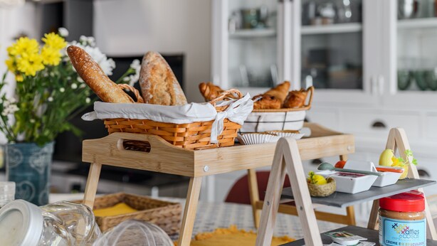 Een houten tafel met broden in manden, een pot pindakaas en een klein schaaltje jam.