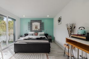 Quarto moderno com cama, mesas de cabeceira, escrivaninha e uma janela grande.