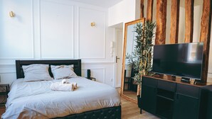 A bedroom with a bed, a TV on a black cabinet, wooden flooring, and a ceiling light fixture. - Spa Du Palais (Rouen)