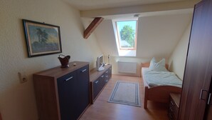 A bedroom with a bed, a dresser, a desk with a computer, a radiator, a window, and a painting on the wall. - Apartment 4 Zum Kuhstall Heinrichsberg - Magdeburg (Heinrichsberg)