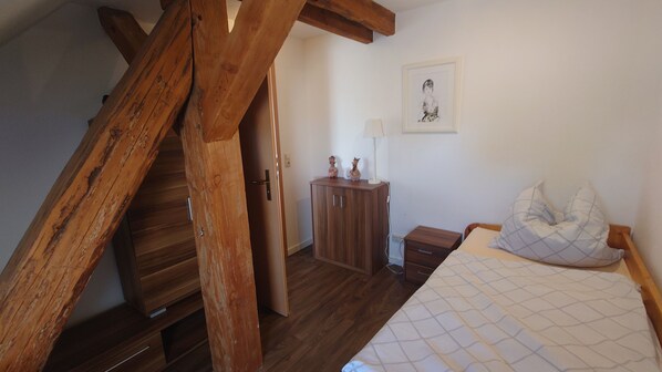 A bedroom with a wooden ceiling, a bed with a quilted cover, a nightstand, a cabinet, and a framed picture on the wall.