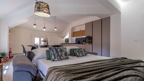 Et moderne soveværelse med en stor seng, en grå sofa og et køkken i baggrunden.