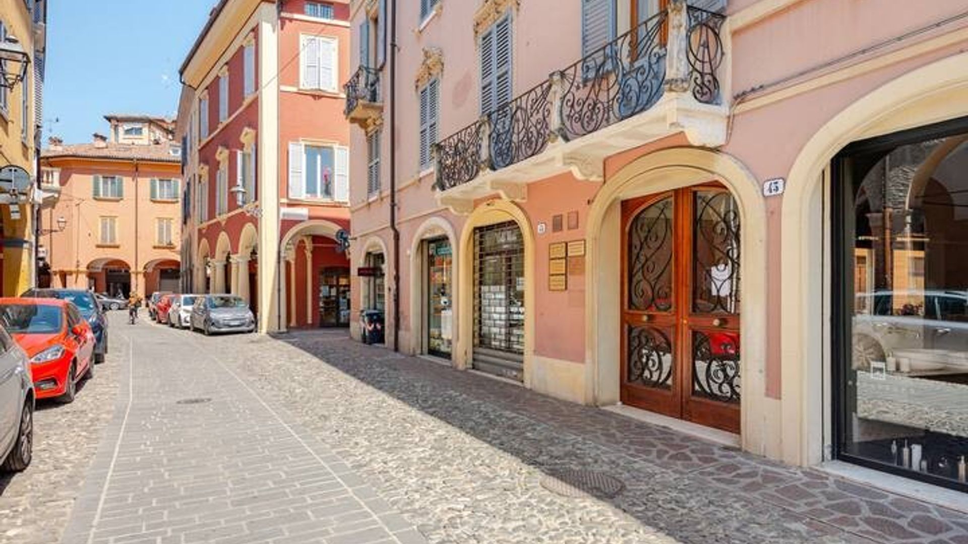 A cobblestone street lined with multi-story buildings, some with visible storefronts and balconies.