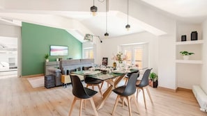 A modern dining area with a glass-top table, black chairs, and a green accent wall.