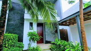 A modern building with a stone facade, a palm tree, and a well-maintained garden with a stone pathway leading to the entrance. - Glenwood Sanctuary Villa 85 Ho Tram (Ho Chi Minh City)