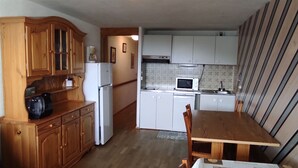 A compact kitchen with wooden cabinets, a refrigerator, a microwave, and a dining table with chairs. - Spacious Apartment in Super Besse for 6 with WIFI (Besse-et-Saint-Anastaise-Super Besse)