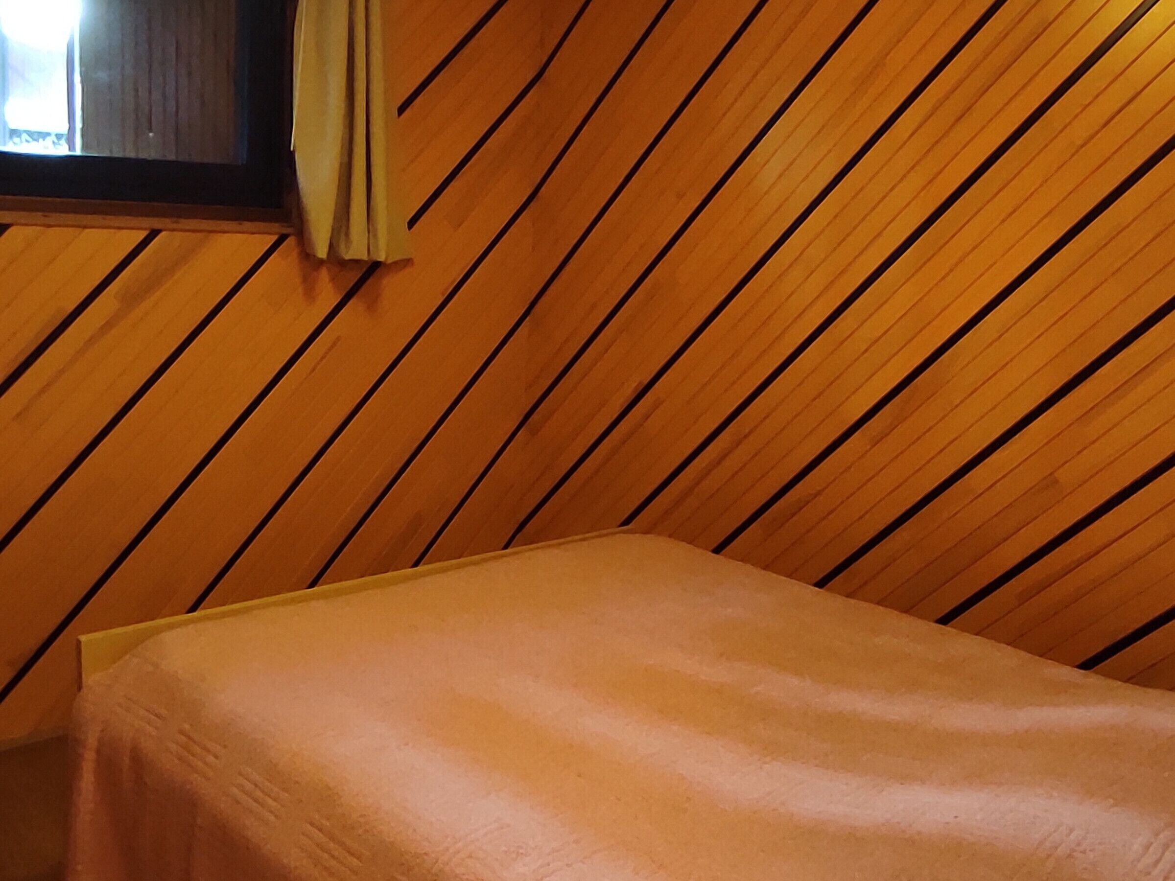 A room with a wooden slatted ceiling and a single bed with a plain mattress.