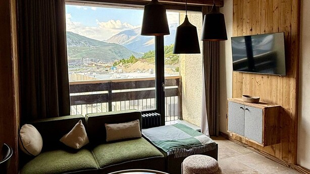 Un salon chaleureux avec un canapé vert, une table basse et un téléviseur fixé au mur.