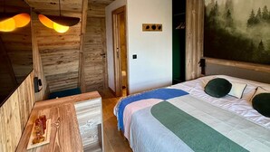 Une chambre confortable avec un plafond en bois, un lit recouvert d’une courtepointe verte et blanche, une table de chevet agrémentée d’un objet décoratif et un tableau représentant une forêt accroché au mur.
