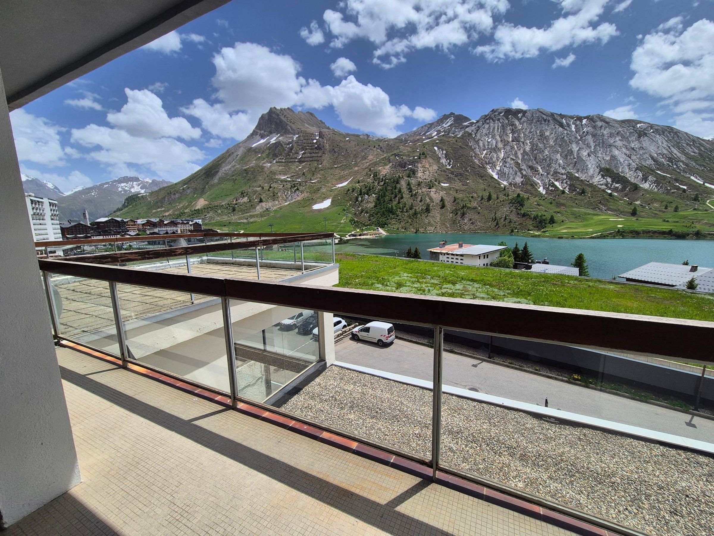 A balcony with a view of a mountain, a lake, and a parking area.