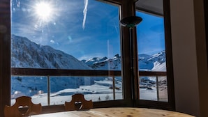 A wooden table with chairs in a room with a large window overlooking a snowy mountain landscape.