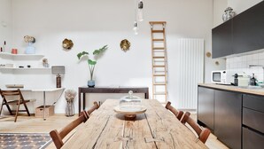 Una cocina moderna con una mesa de comedor de madera, electrodomésticos integrados y detalles decorativos en la pared.
