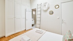 Un dormitorio con cama, armario blanco y baño a la vista a través de una puerta abierta.