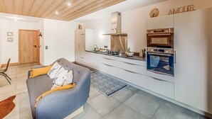 Eine moderne Küche mit Edelstahlgeräten, einer Holzbalkendecke und einem grauen Sofa mit Kissen.