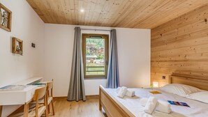 Ein Schlafzimmer mit Holzboden, einem Bett mit weißen Leinentüchern, einem Schreibtisch mit Stuhl und einem Fenster mit Vorhängen.