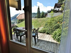 A wooden deck with outdoor furniture, a view of a mountainous landscape, and a building with a sloped roof.