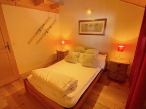 A bedroom with a bed, two bedside tables, a nightstand, a framed picture on the wall, and a door with a towel hanging on it.