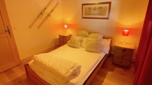 A bedroom with a bed, two bedside tables, a nightstand, a framed picture on the wall, and a door with a towel hanging on it.