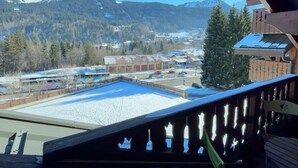 A view from a balcony overlooking a snow-covered area with buildings and mountains in the background.