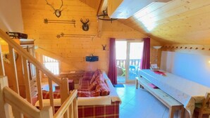 A cozy cabin interior with a loft bed, a sofa, a dining table, and a staircase.