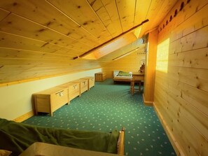 A small attic bedroom with a sloped ceiling, wooden walls, a green patterned carpet, a bed, a desk, and built-in wooden storage units.