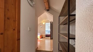 Un pasillo que conduce a un dormitorio con una cama, una mesita y una estantería en la pared.
