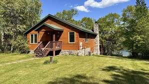 Une cabane en rondins avec une cheminée en pierre, une terrasse en bois et une vue sur un lac.