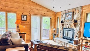 L’intérieur chaleureux d’un chalet avec des murs en bois, une cheminée en pierre, un téléviseur et un coin salon confortable.