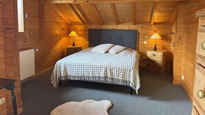 Un dormitorio de cabaña de madera acogedor, con una cama, dos mesitas de noche con lámparas, un radiador y una pequeña alfombra.