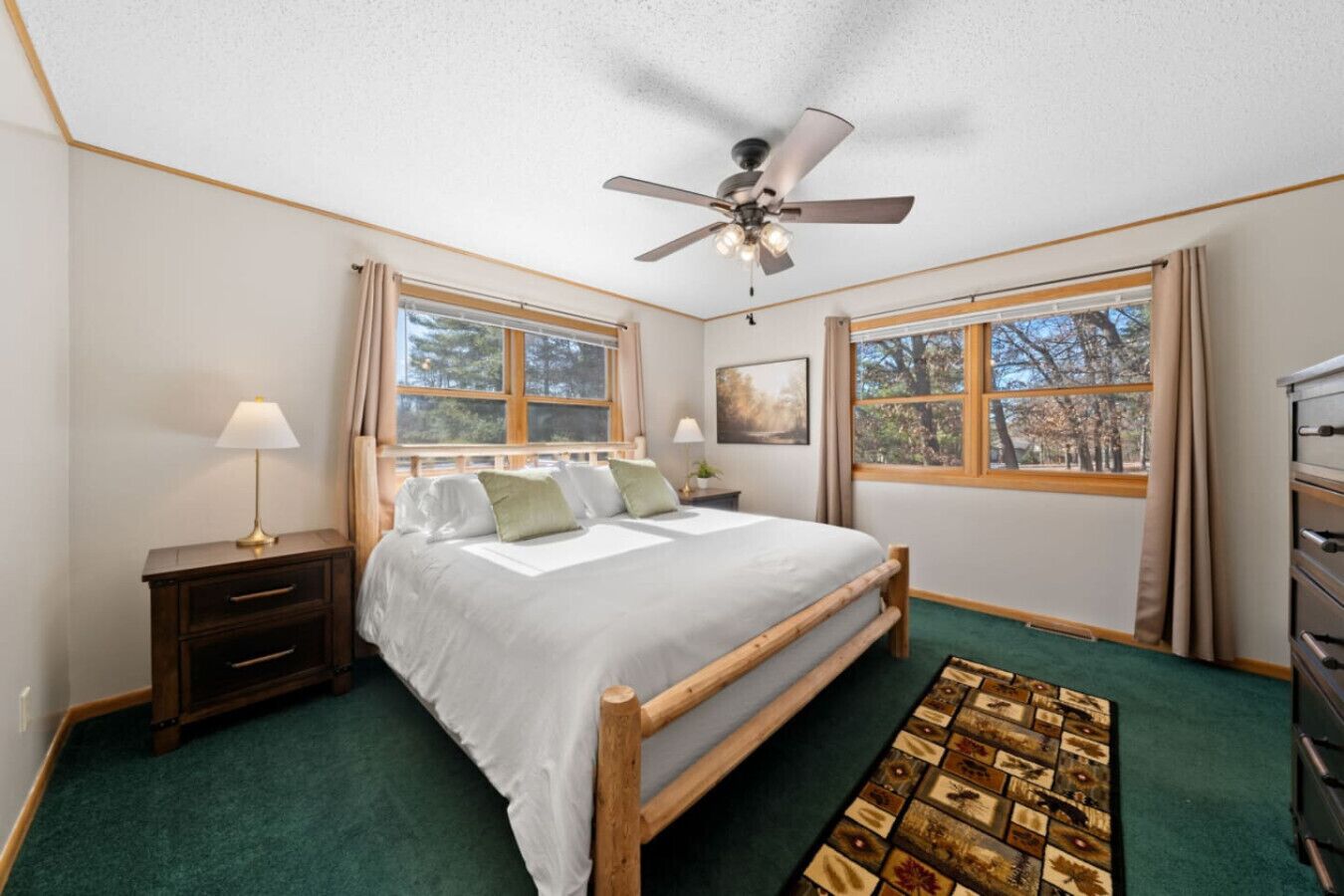 Une chambre à coucher avec un lit, des tables de chevet, un ventilateur de plafond et de grandes fenêtres.