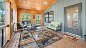 A covered porch with wooden flooring, a green sofa, a chair, and a coffee table.