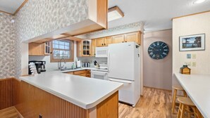 A modern kitchen with wooden cabinets, a white refrigerator, and a large island.