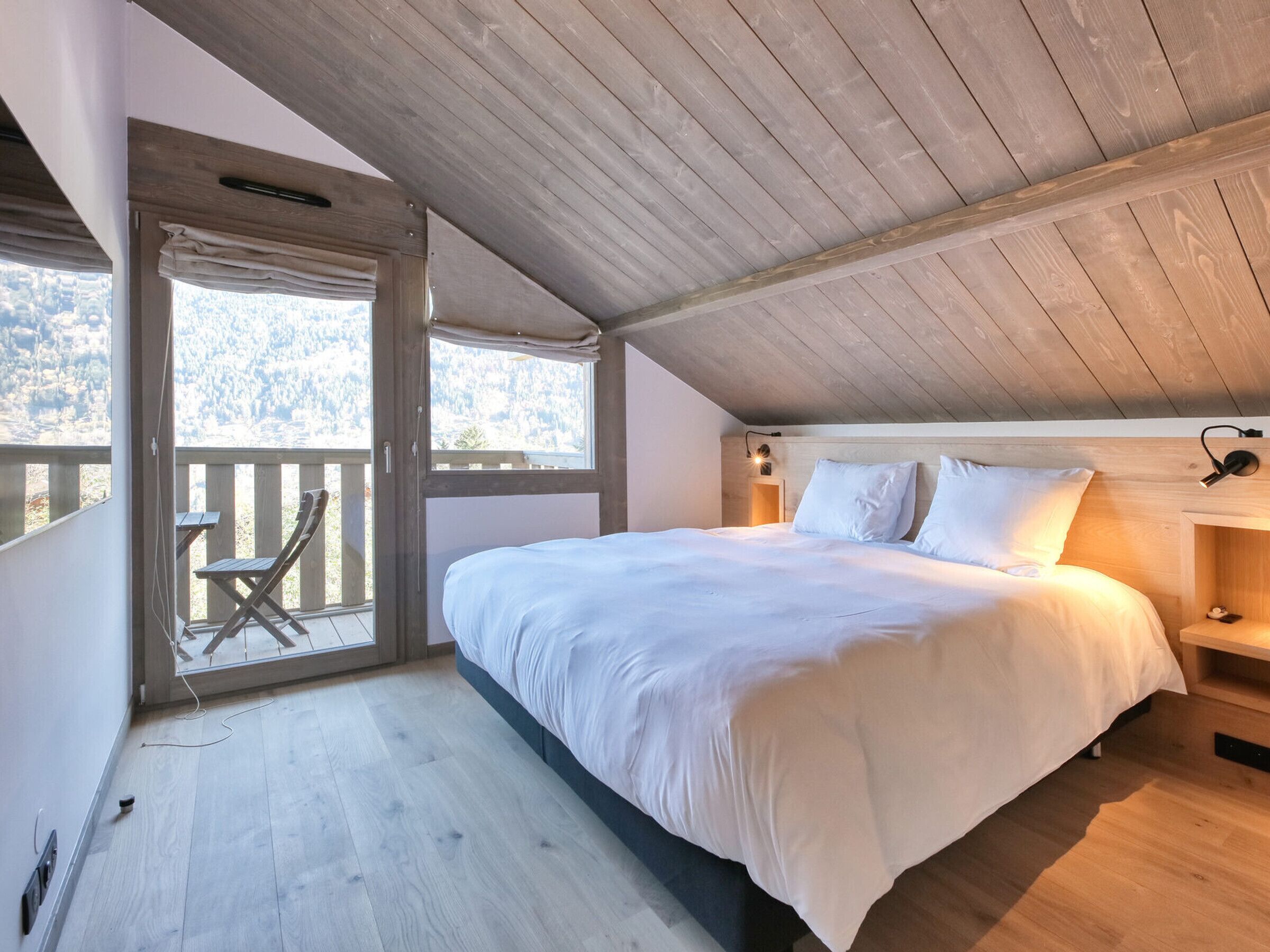A bedroom with a large bed, wooden ceiling, and a balcony with a chair.