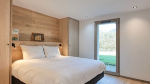 Una camera da letto moderna con un letto grande, una testata in legno e vista su un paesaggio verde attraverso una porta scorrevole.